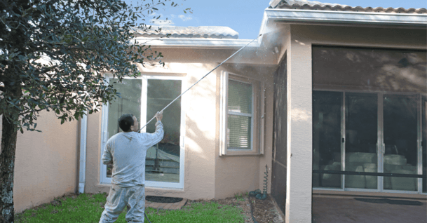 Painter cleaning exterior of home with a power washer hose and getting the gutters on a roof.