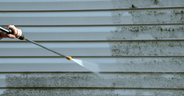 Person power washing dirt off the side of a house.