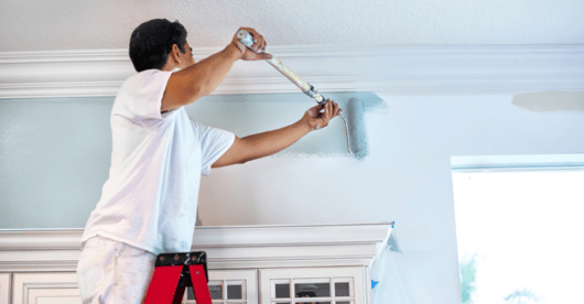 Painter painting a wall above kitchen cabinets a light blue shade.