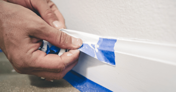 Person peeling tape from baseboards to protect walls from paint.