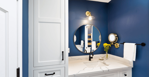 Small bathroom with dark blue walls and white cabinets and countertops.