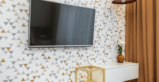 Interior bedroom with white wallpaper with triangles and a tv mounted on the wall.
