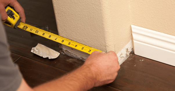 Person measuring small pop out wall inside a room to paint the basebaords.