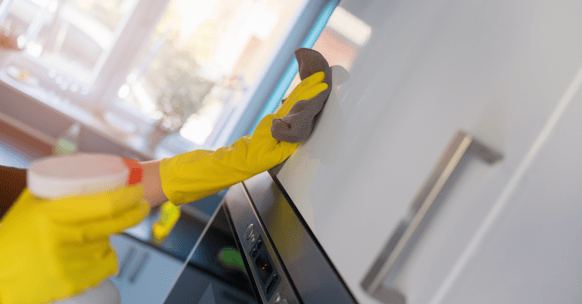 Person wiping down kitchen cabinets with a spray and a cloth to clean it.