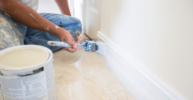 Painter brushing white paint on baseboards inside of a home in Omaha, NE.