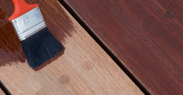 Brush staining a wood deck a dark brown color.