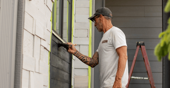 Painter brushing black paint on outside siding of a home in Omaha, NE.