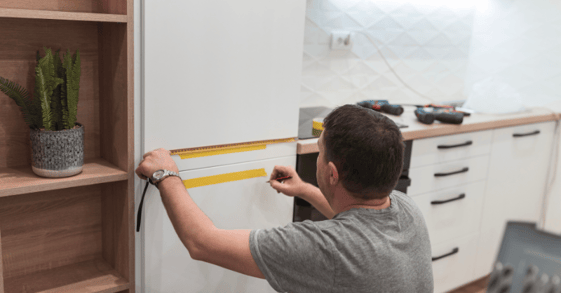Man measuring white kitchen cabinets with measuring tape to get a painting quote.