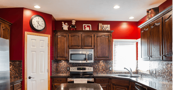 Kitchen with red walls and toned cabinets and chef inspired decor above the upper cabinets.