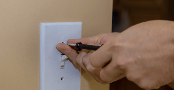 Person removing interior light switch cover from yellow wall to paint.