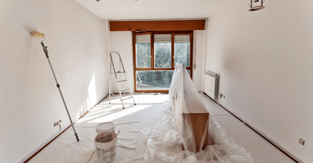 Empty room with paint supplies around the floor and taping with windows open before and during painting.