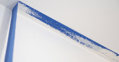 Blue painters tape being peeled off a ceiling after the walls were painted white.