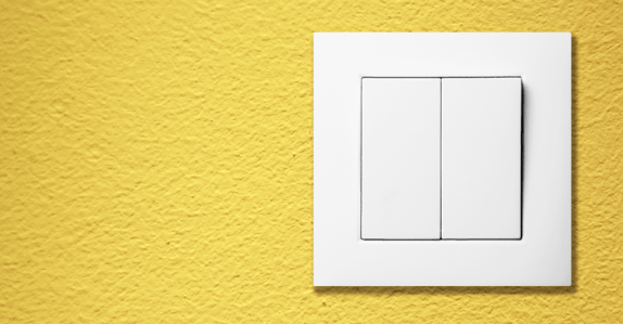 Interior white light switch cover on bright yellow wall.