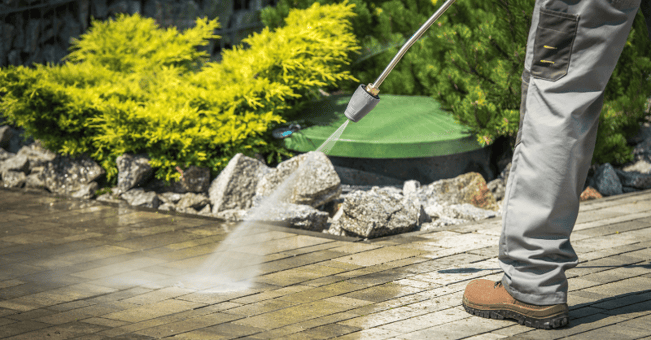 Person power washing their driveway and garden concrete area to clean it.