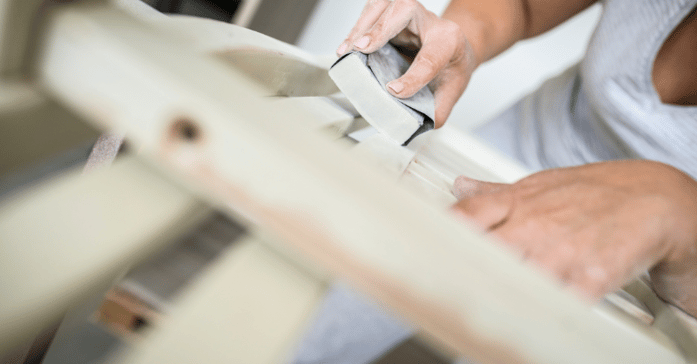 Painter using a sanding block on wooden furniture before varnishing.