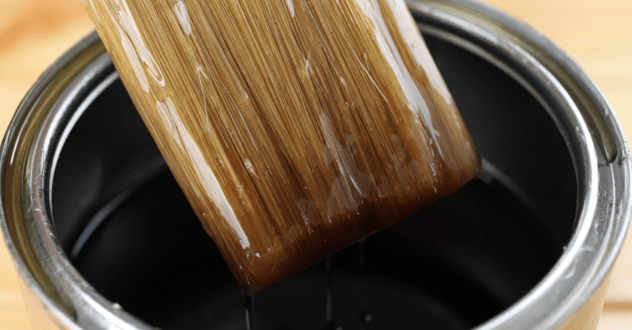 Dark varnish in a paint can with a bristled brush dipped inside.