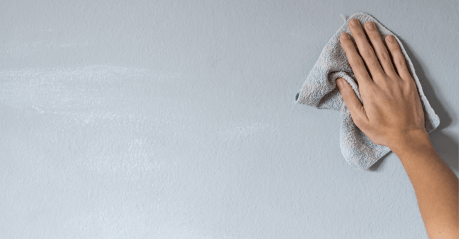 hand wiping down walls painted light bluewith a rag.