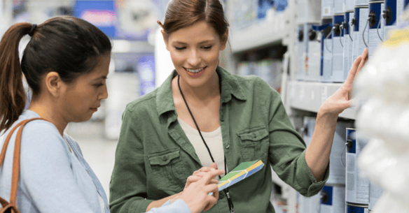 Two women comparing paint colors in a paint store next to paint cans.