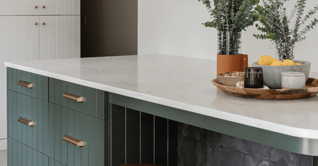 Kitchen cabinet island with a white countertop and dark green cabinet island with gold handles.