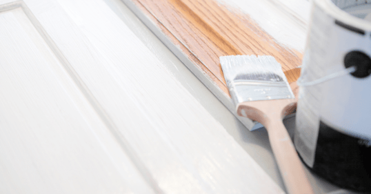 Close up image of cabinet door with a paint gallon and brush dipped in white paint on top.