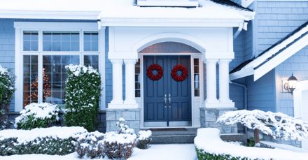 Front of home with blue exterior paint and snow on the ground and on bushes..