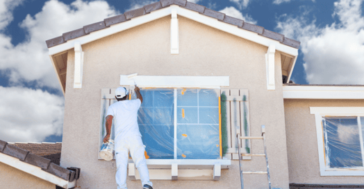 Man painting window frames on the exterior of a home.