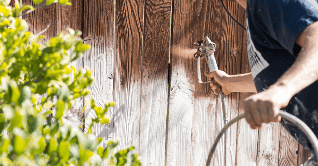 Painter staining wood fence a dark brown opaque stain in Omaha, NE.