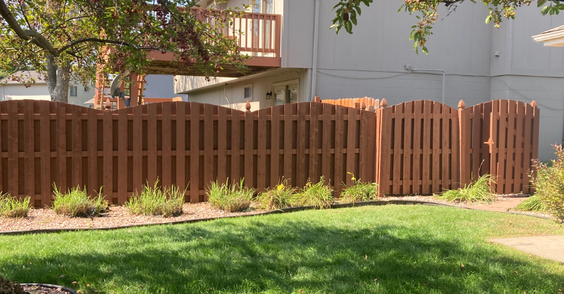 Warm brown stained fence with curves along the tops of the wood boards.