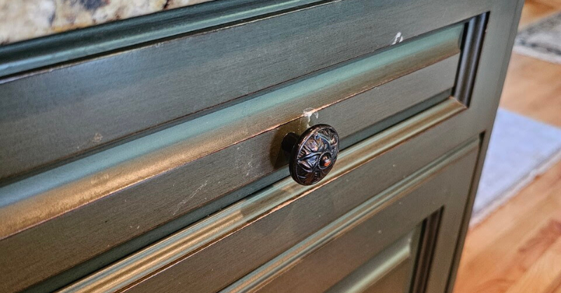 Cabinet drawer with chipping cabinet paint that is a dark muted green color with an antique bronze knob.