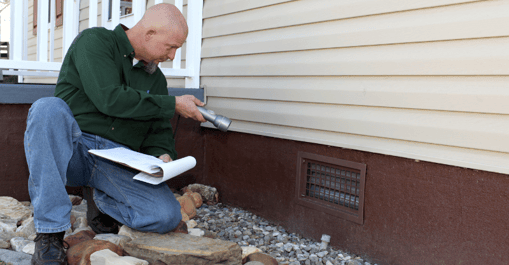 Man inspecting vinyl siding with a flashlight.