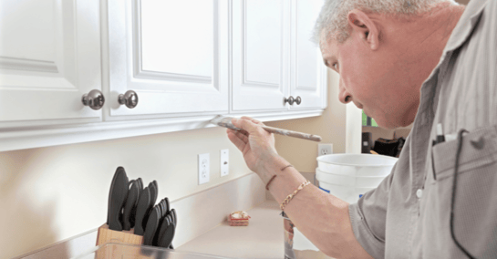 Cabinet painter in Omaha touching up white cabinet door with white paint.