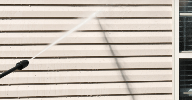 Power washer spraying the exterior siding of a house before painting.