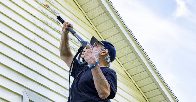 Painter power washing exterior of house painted white to clean it before listing it for sale in omaha, Ne.