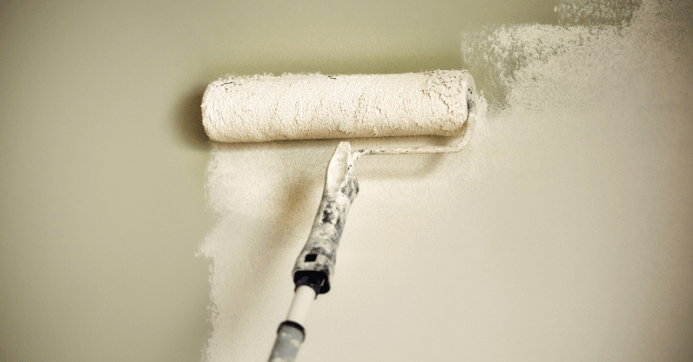 Paint roller with white paint against a sage green wall.