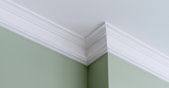 White interior crown molding next to wall corner painted sage green and white ceilings.