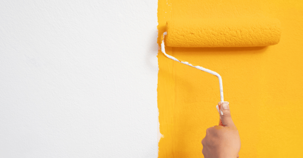 Bright yellow paint being rolled onto a white wall.