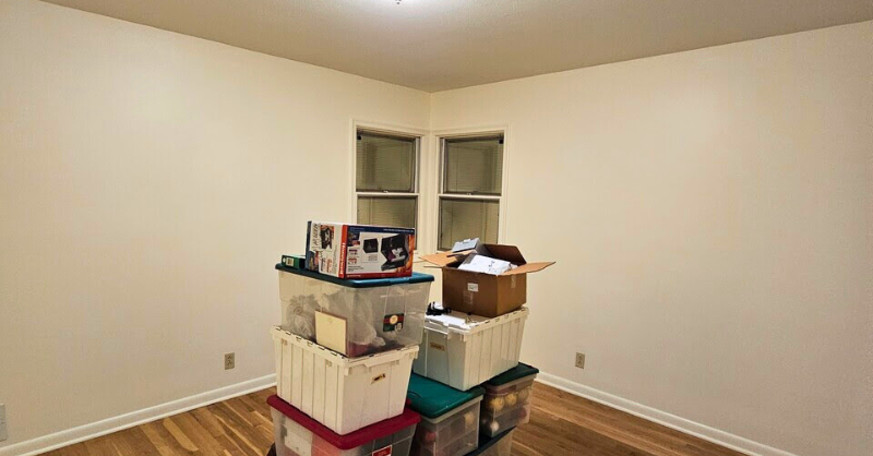 Room with freshly painted white walls, trim, and ceiling and boxes and totes in the middle of the room.