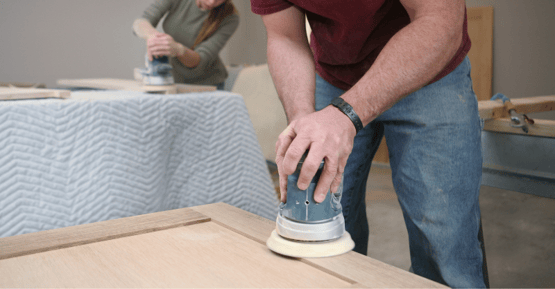 Man sanding cabinet door with a electric sander before diy painting cabinets.