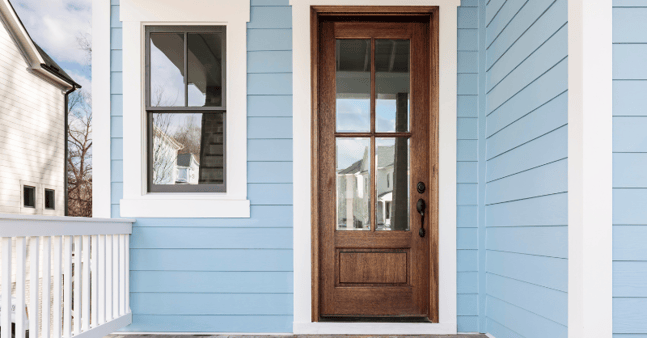Exterior of a home with baby blue siding, white trim, and a dark wood stained exterior door.