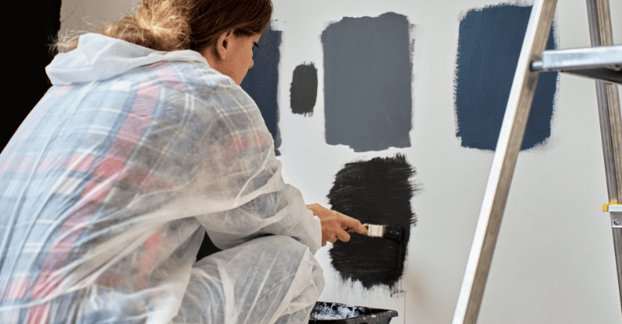Woman testing dark blue and grey paint colors on a wall in her home in Omaha, NE.