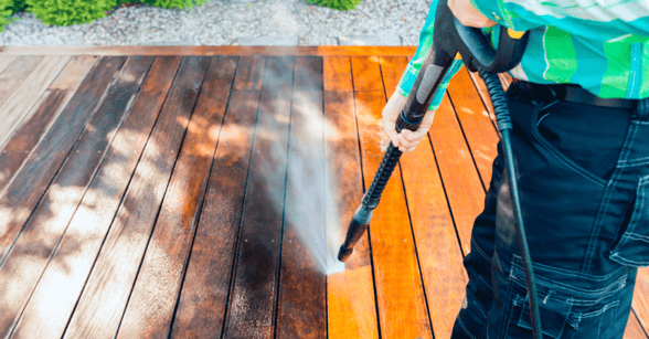 Person cleaning wooden deck boards with a power washer.