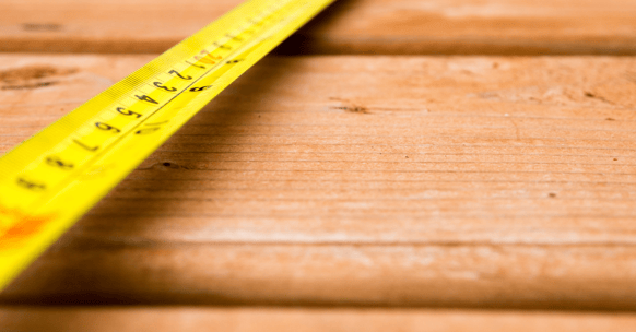 Close up of warm colored wooden deck boards with a yellow tape measure laid out overtop of it.