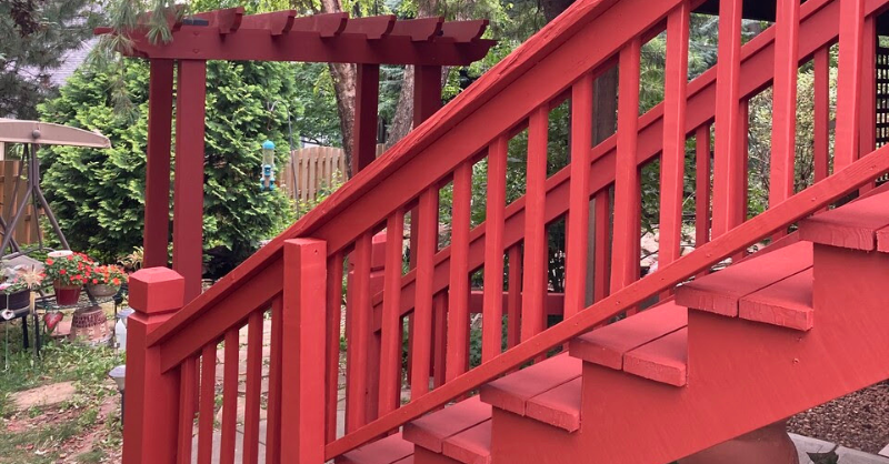 Deck stained a bright red color with a solid stain with stairs and a pergola.