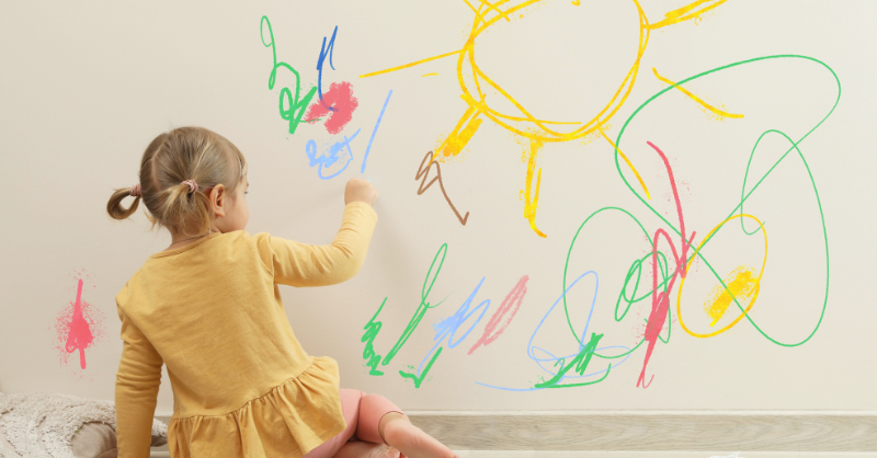 Girl drawing on interior wall with crayon.