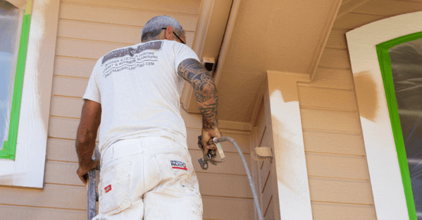 Brush & Roll Painting painter spraying beige paint onto exterior of house in Omaha, NE.