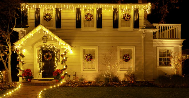 Warm white and yellow chrsitmas lights along the roofline and peak of a home with garlands and wreaths in Omaha, NE.