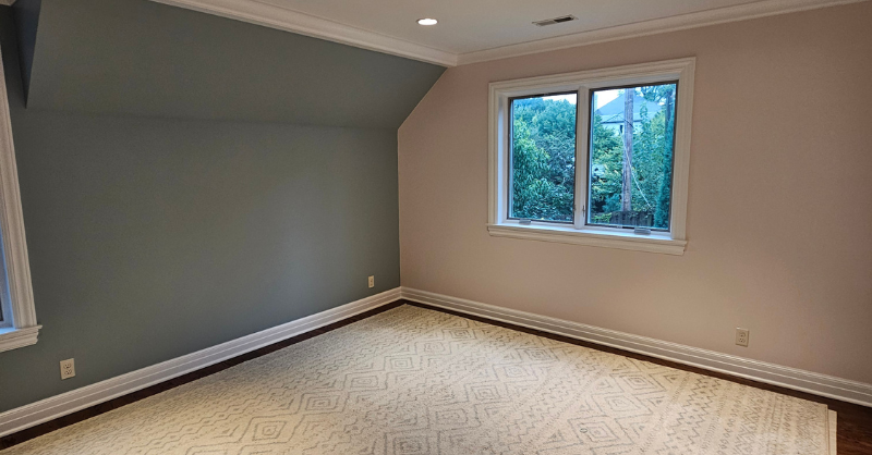 Bedroom with one wall painted a dark sage green and another wall painted a light pink paint color with white trim and ceiling in Omaha, NE.