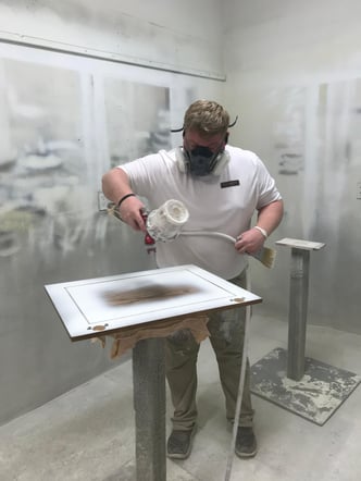 Brush & Roll Painting painter spraying a cabinet door with white paint in a spray booth.