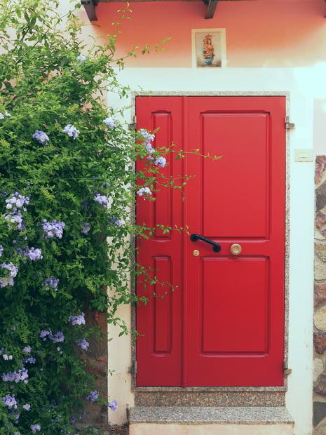 Red front door with bright green bushes to the side.