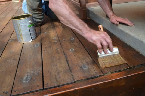 Painter back brushing stain into a wood deck in Omaha.